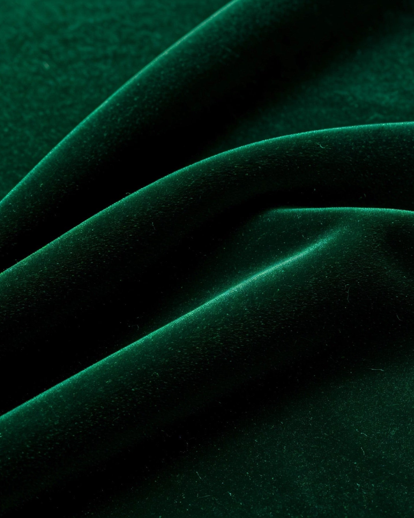 Close-up of green velvet fabric arranged in soft folds, showing its smooth surface and subtle sheen.