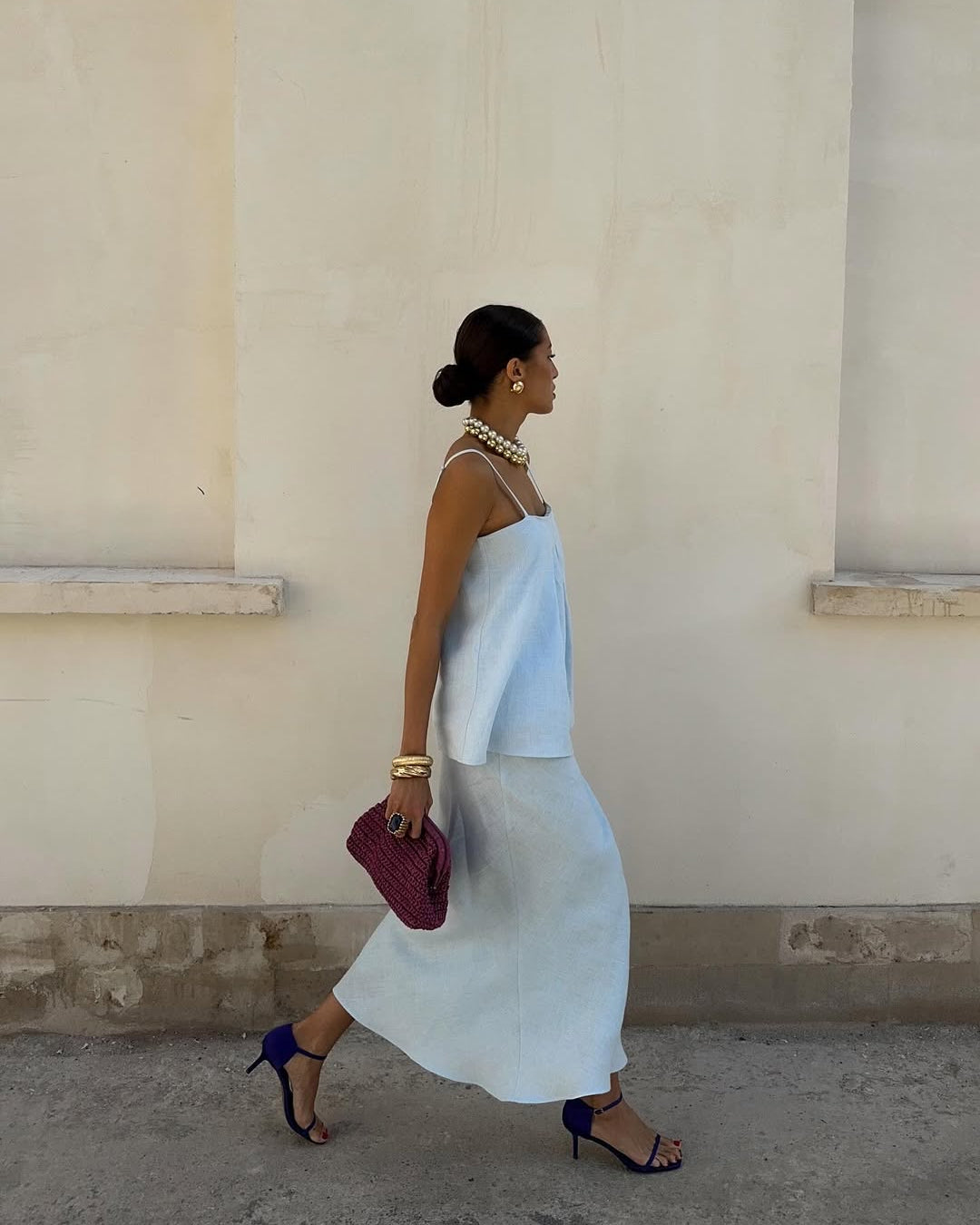 Woman in a light blue dress walking past a beige wall.