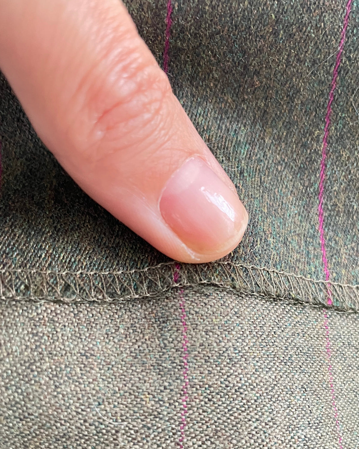 Close-up of a a seam on a textured wool green fabric with thin purple pinstripes.
