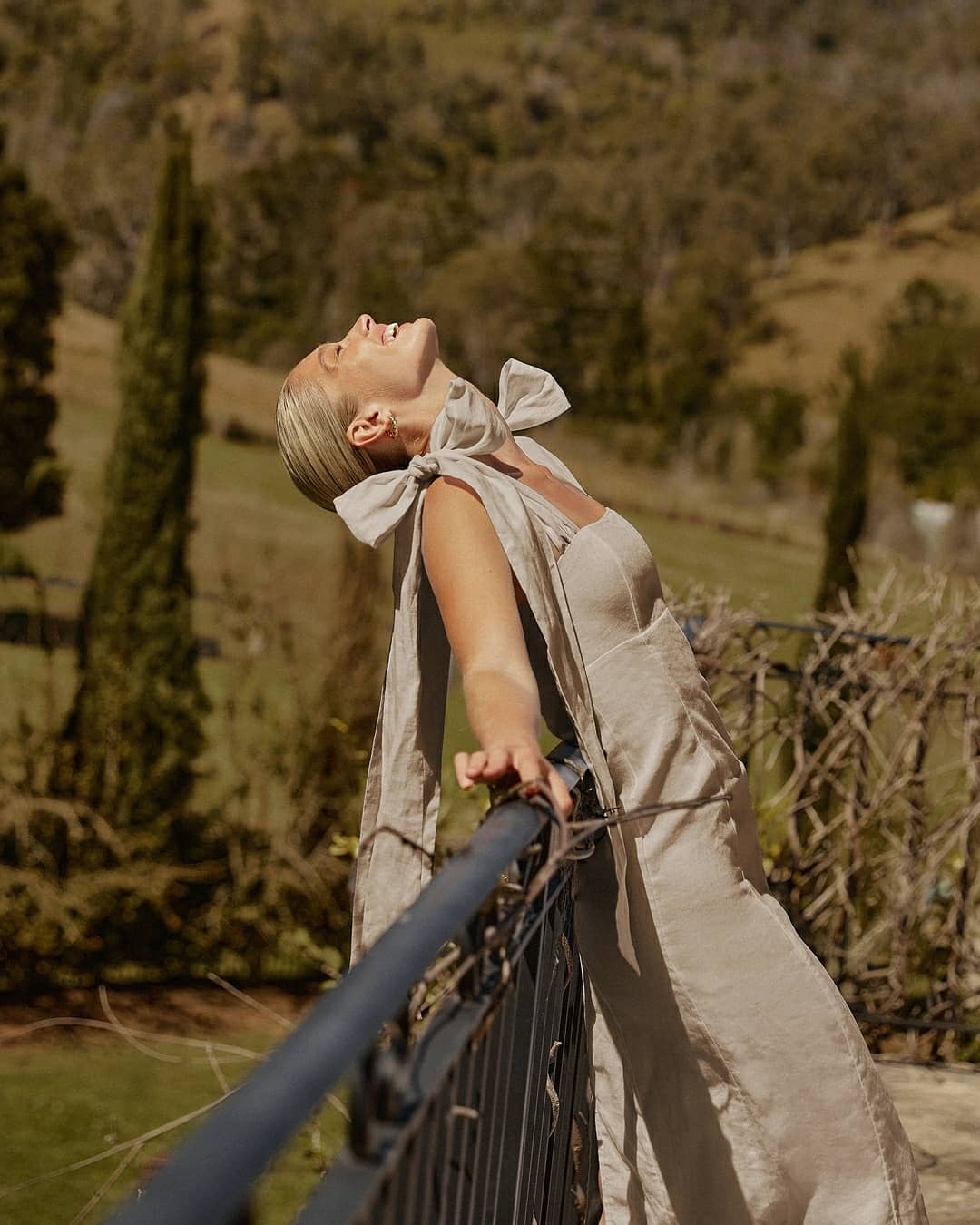 Woman wearing a beige linen midi dress with long shoulder bows outdoors