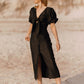 Woman in a black dress standing on a sandy beach.