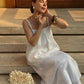 A woman wearing a white linen top sits on stone steps outdoors.