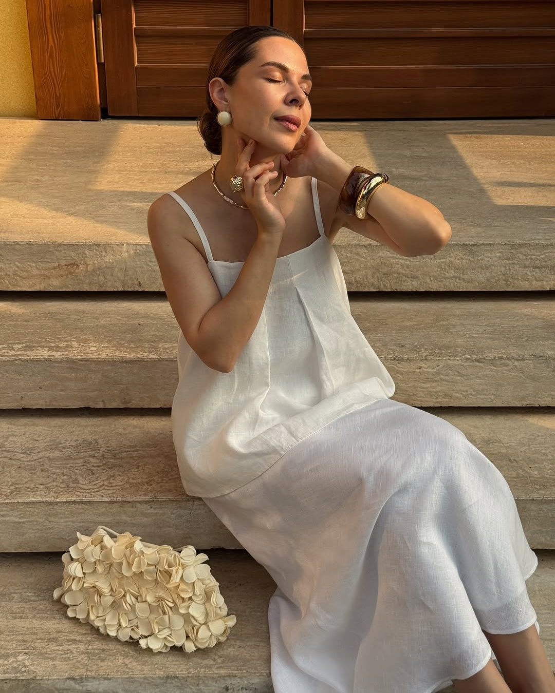 A woman wearing a white linen top sits on stone steps outdoors.