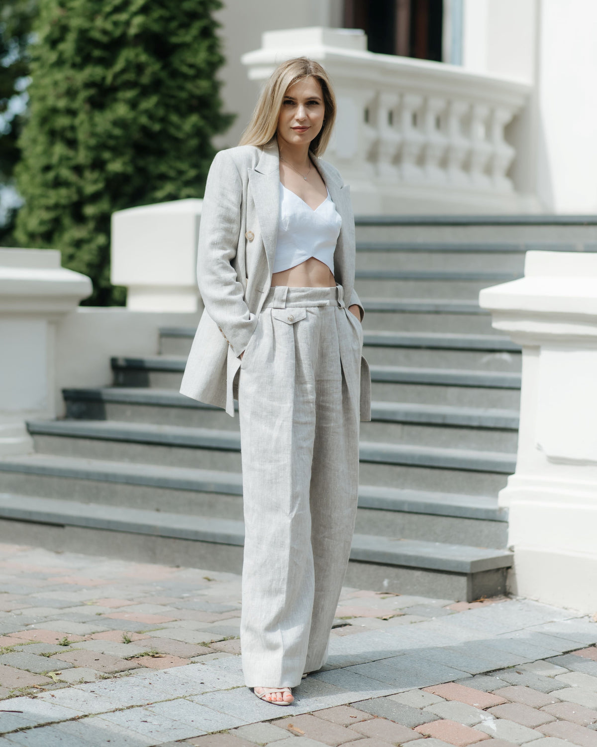 Woman standing in beige wide-leg linen trousers with a high waist and double front pleats, styled with a matching linen blazer