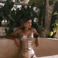 Woman in a beige silk slip dress sitting on a stone bench