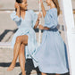 Two women on beach swings wearing sky blue linen and muslin midi wrap dresses.