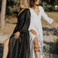 Two women in black and white dresses standing on a sandy path with trees in the background.