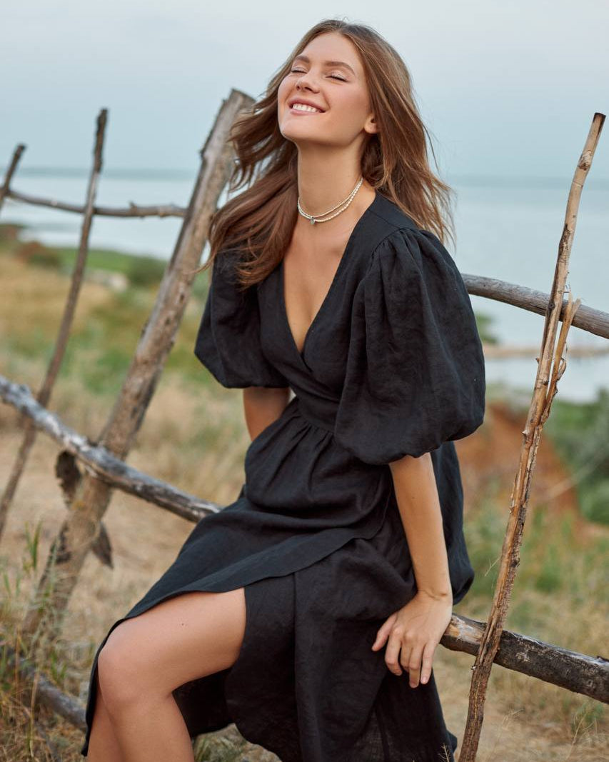 Woman in a black wrap  dress sitting on a wooden fence with a scenic background