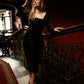 Woman in a brown velvet dress beside an ornate railing, showing the square neckline and long fitted sleeves.