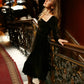 Full-length view of a woman wearing a brown velvet midi dress with long sleeves beside an ornate staircase railing.