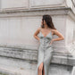 Woman in a sage silk slip dress standing against a stone wall.