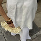 A person wearing a loose white linen  top and white skirt, holding a cream flower bouquet.