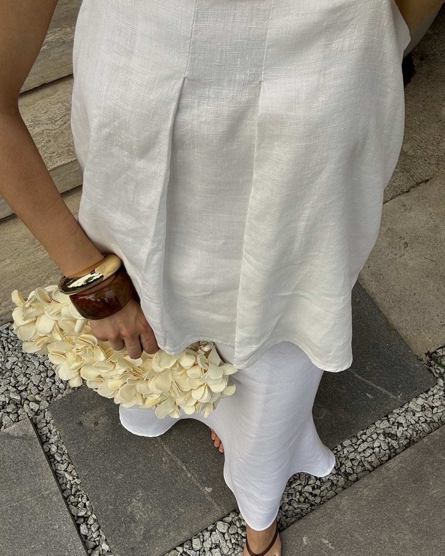 A person wearing a loose white linen  top and white skirt, holding a cream flower bouquet.