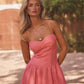 Woman wearing a  coral linen corset midi dress with fitted bodice and thin straps standing outdoors with a blurred background