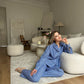 A woman sitting on a white sofa wearing a blue cotton suit with pants and a shirt.
