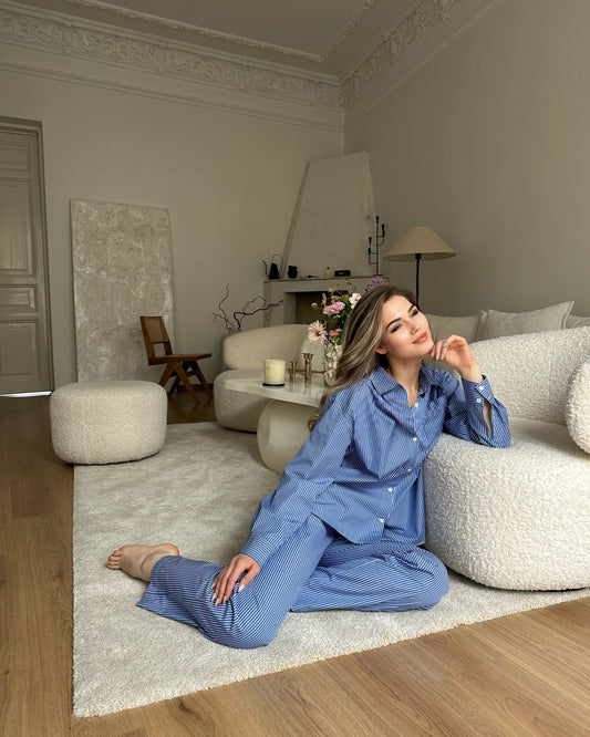 A woman sitting on a white sofa wearing a blue cotton suit with pants and a shirt.