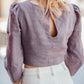 Person wearing a light purple blouse with puffed sleeves and a cutout back detail, standing outdoors.