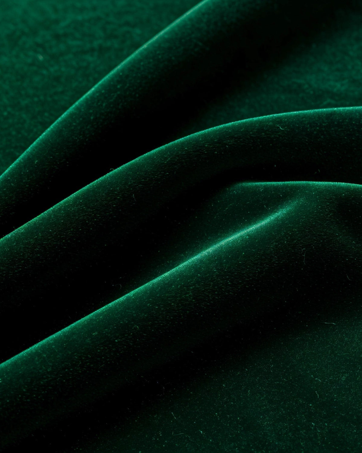 Close-up of green velvet fabric arranged in soft folds, showing its smooth surface and subtle sheen.