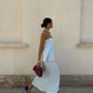 Woman in a light blue dress walking past a beige wall.