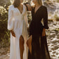 Two women in long dresses standing on a sandy path with natural scenery.