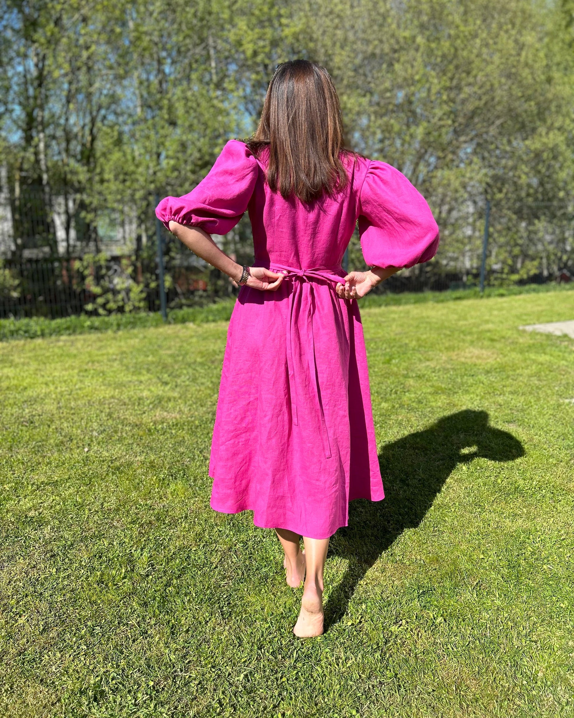 Person wearing a fuchsia dress standing on grass with trees in the background