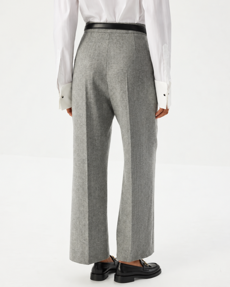 A person shown from the back wearing mid-rise waist ,  straight-leg  gray trousers with a black belt, a white shirt, and black loafers. 