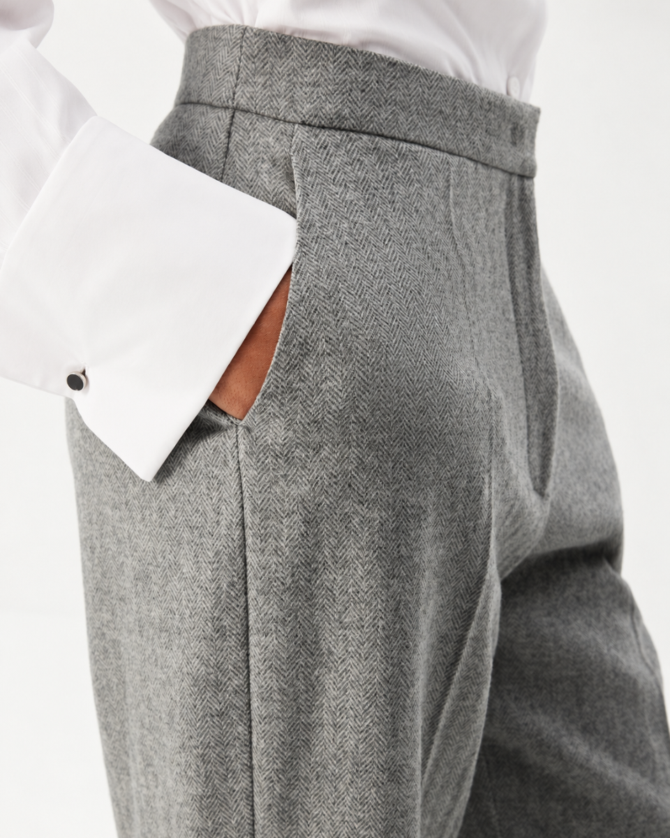 Close-up of a person wearing gray herringbone trousers with a white dress shirt and a brown leather pocket showing.