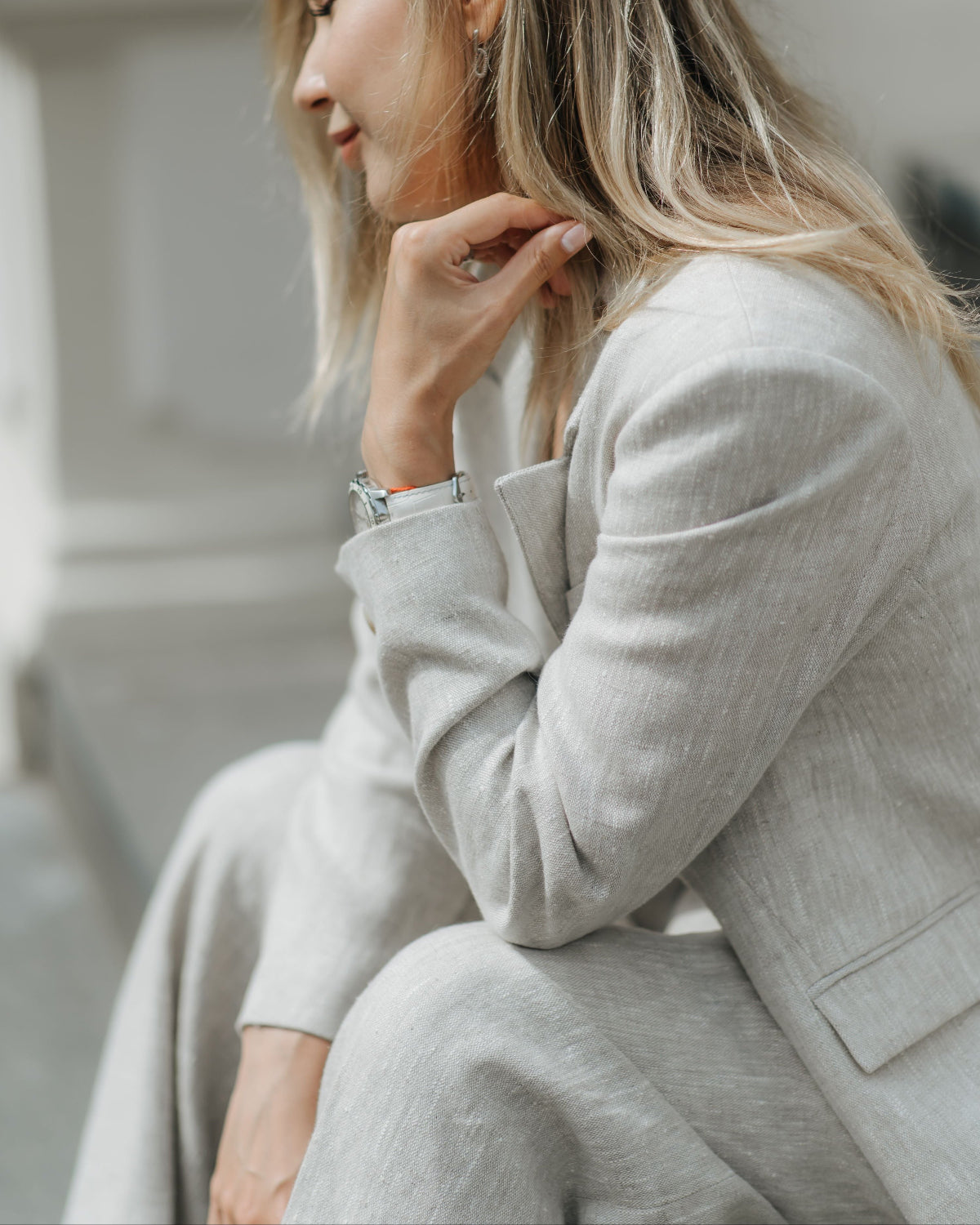 Close side view of a seated woman wearing heavyweight beige linen trousers with a matching linen blazer