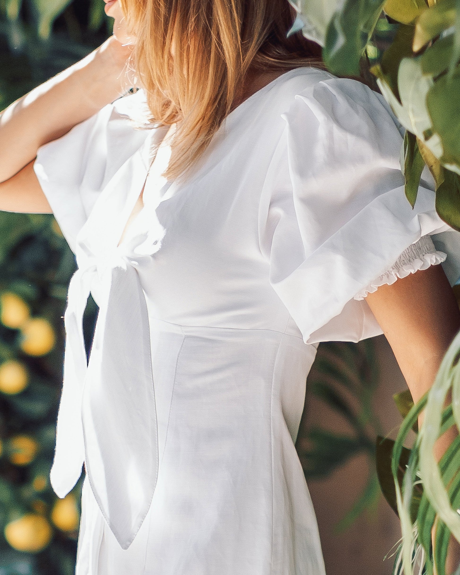Woman wearing a white dress with ruffled sleeves in a garden setting