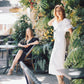 Two women in an outdoor setting with plants and tables.