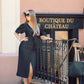 Woman in a black dress standing in front of 'Boutique du Château' sign.