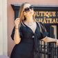 Woman in a black outfit with sunglasses standing in front of a boutique sign.