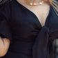 Navy blue top with a bow detail worn by a person, with a blurred background