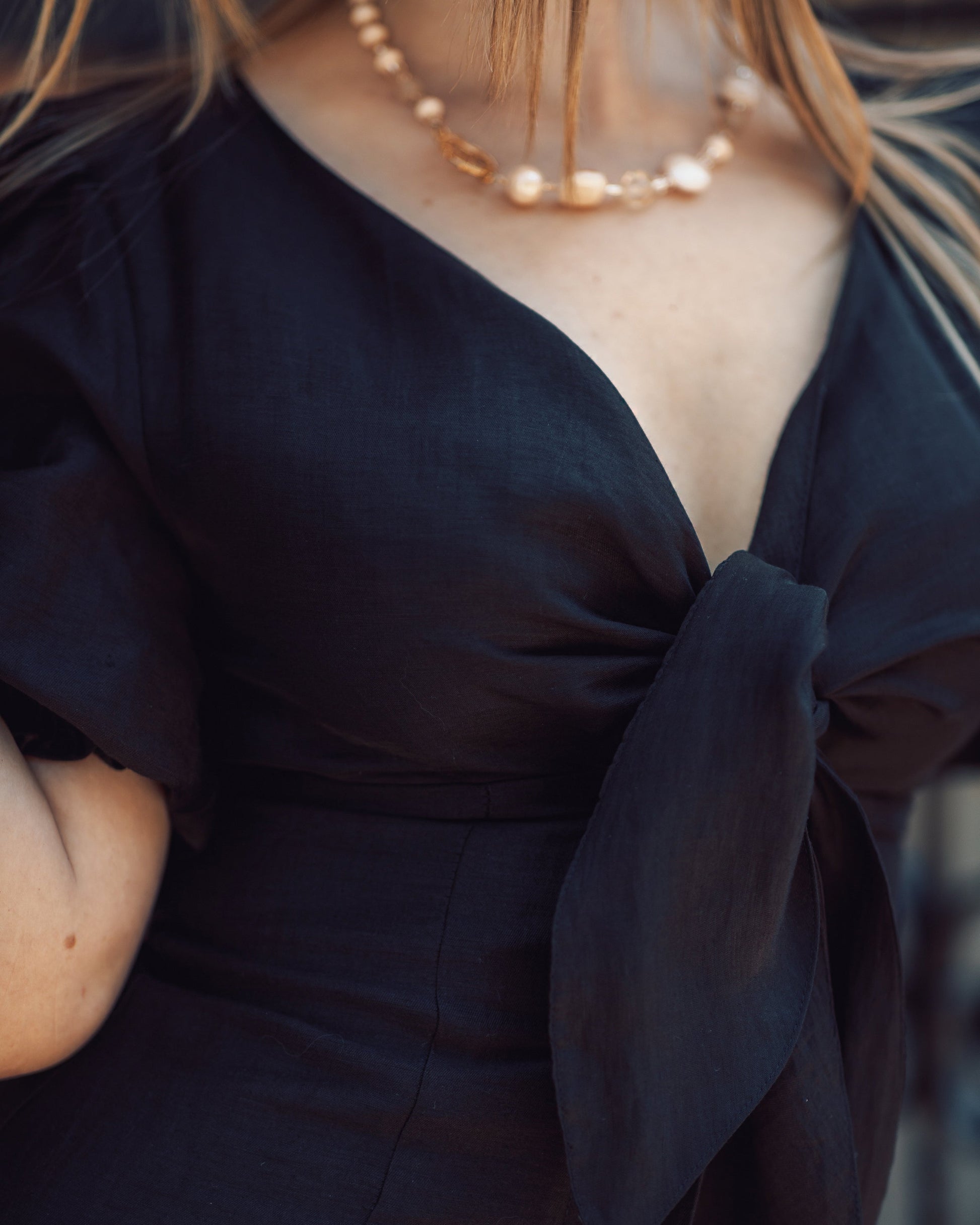 Navy blue top with a bow detail worn by a person, with a blurred background