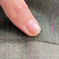 Close-up of a a seam on a textured wool green fabric with thin purple pinstripes.