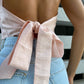 Close-up of a blush pink linen backless top, showing the open back and long bow tie at the waist.