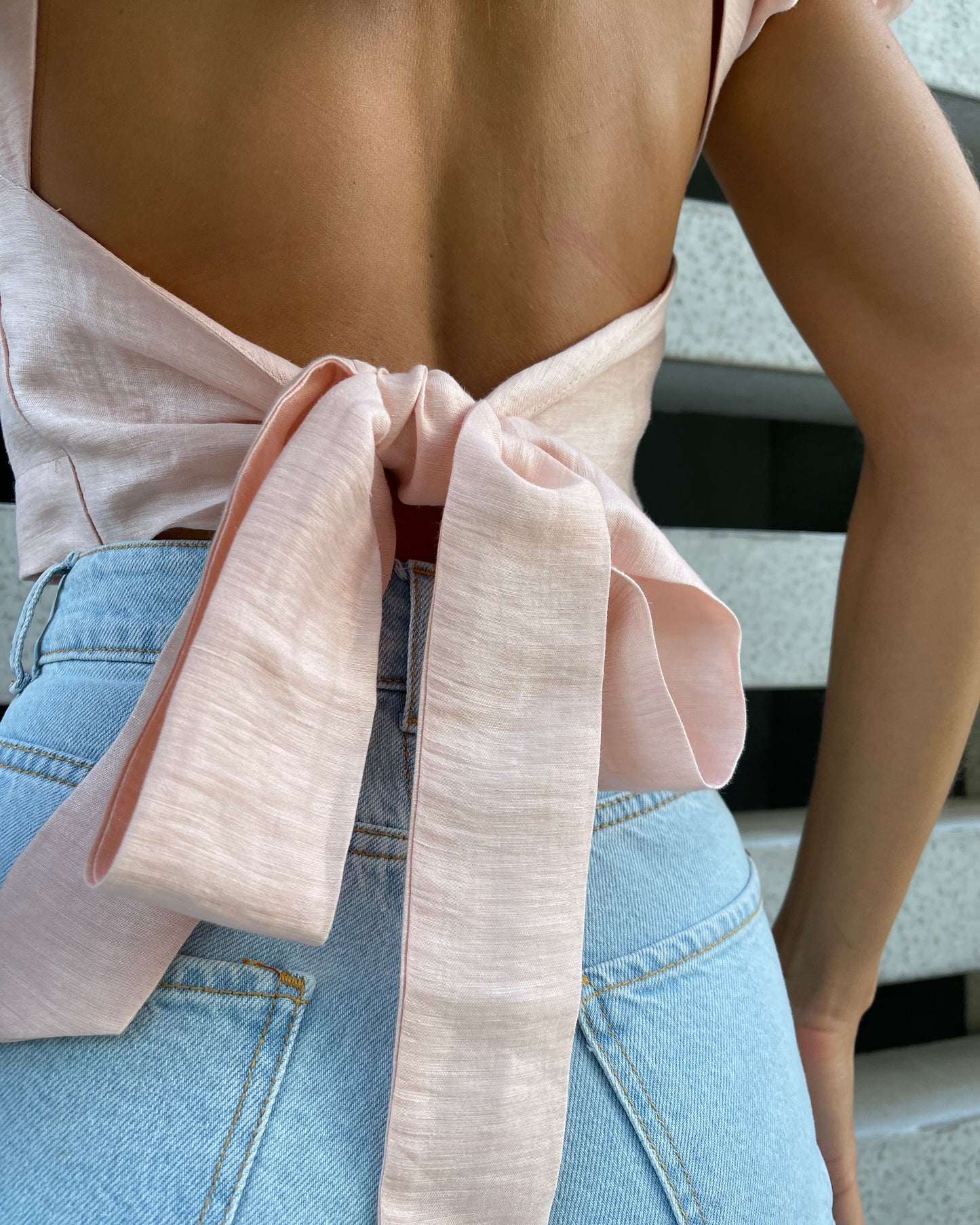 Close-up of a blush pink linen backless top, showing the open back and long bow tie at the waist.