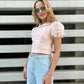Woman wearing the blush pink LUNA linen top with puff sleeves and high-waisted jeans, showing its fitted cropped silhouette from the front.