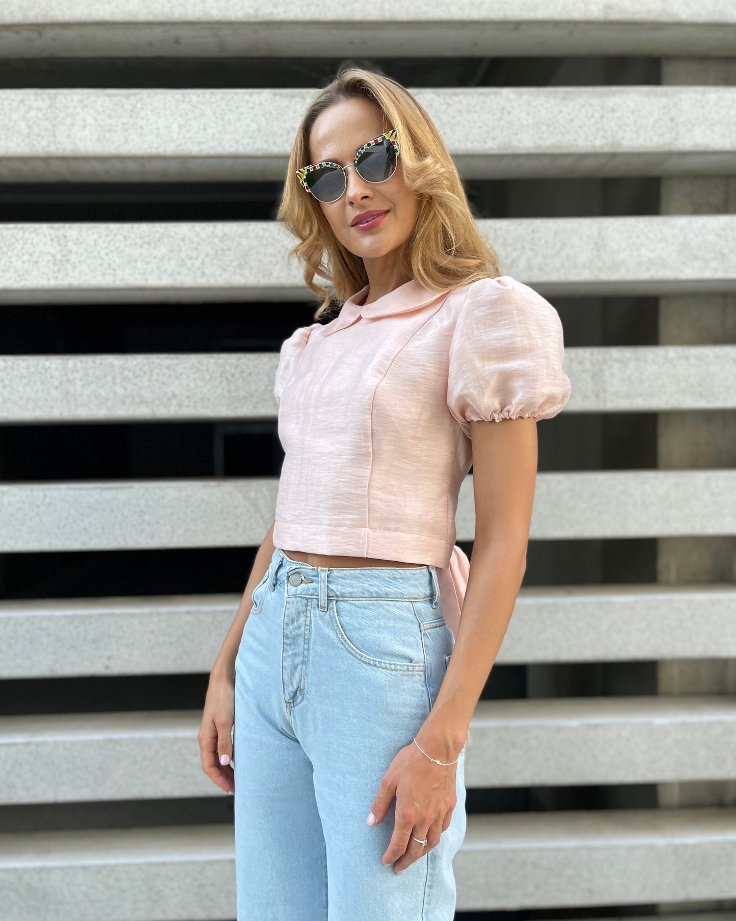 Woman wearing the blush pink LUNA linen top with puff sleeves and high-waisted jeans, showing its fitted cropped silhouette from the front.