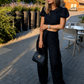 Woman wearing the LUNA black backless linen top with wide-leg trousers on a sunlit city street, styled as an elegant summer outfit.