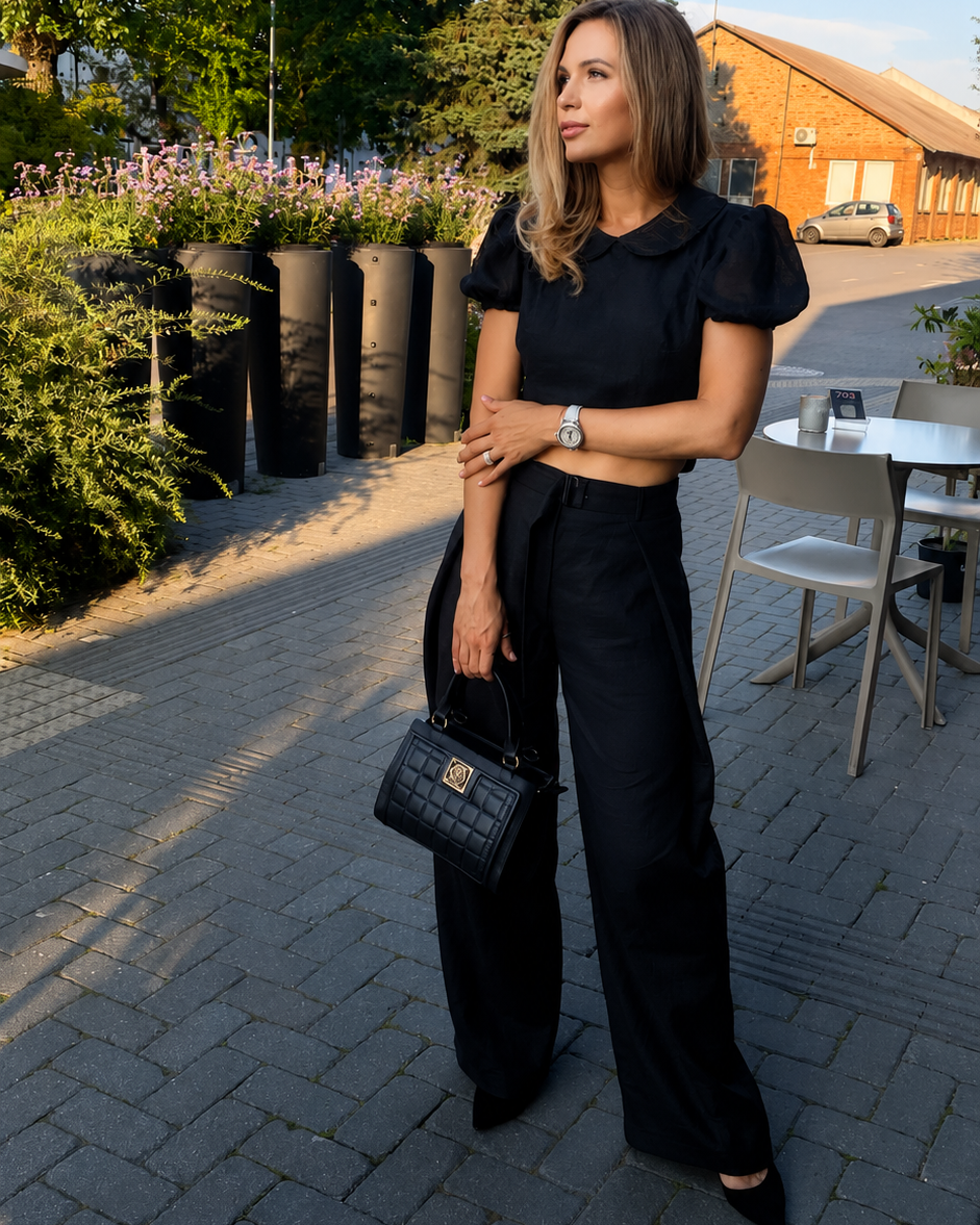 Woman wearing the LUNA black backless linen top with wide-leg trousers on a sunlit city street, styled as an elegant summer outfit.