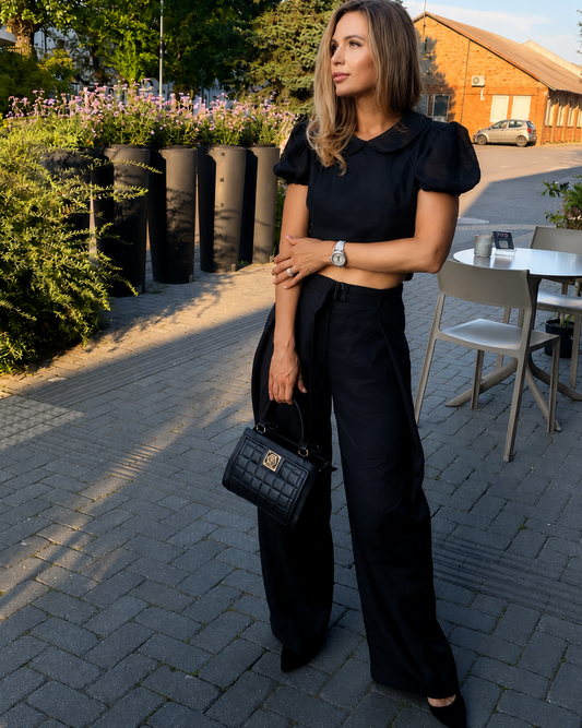 Woman wearing the LUNA black backless linen top with wide-leg trousers on a sunlit city street, styled as an elegant summer outfit.