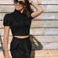 Woman in the LUNA black linen crop top with puff sleeves and a high neckline, styled with matching black trousers in warm sunlight.