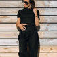 Woman wearing the LUNA black linen crop top with matching wide-leg linen trousers, creating a minimal all-black summer outfit in the sunlight.