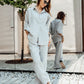 A woman wearing a light grey linen suit with a relaxed fit. The suit includes a shirt with a classic collar and 3/4 sleeves, and trousers with a high-rise waist and side pockets.