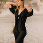 A woman standing on a beach wearing a black midi dress with puff sleeves and a knot front detail.