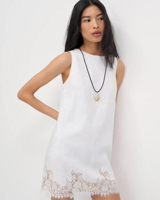 Woman wearing a white dress with lace details on a plain background