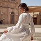 Woman in a white dress sitting on steps with a desert building in the background