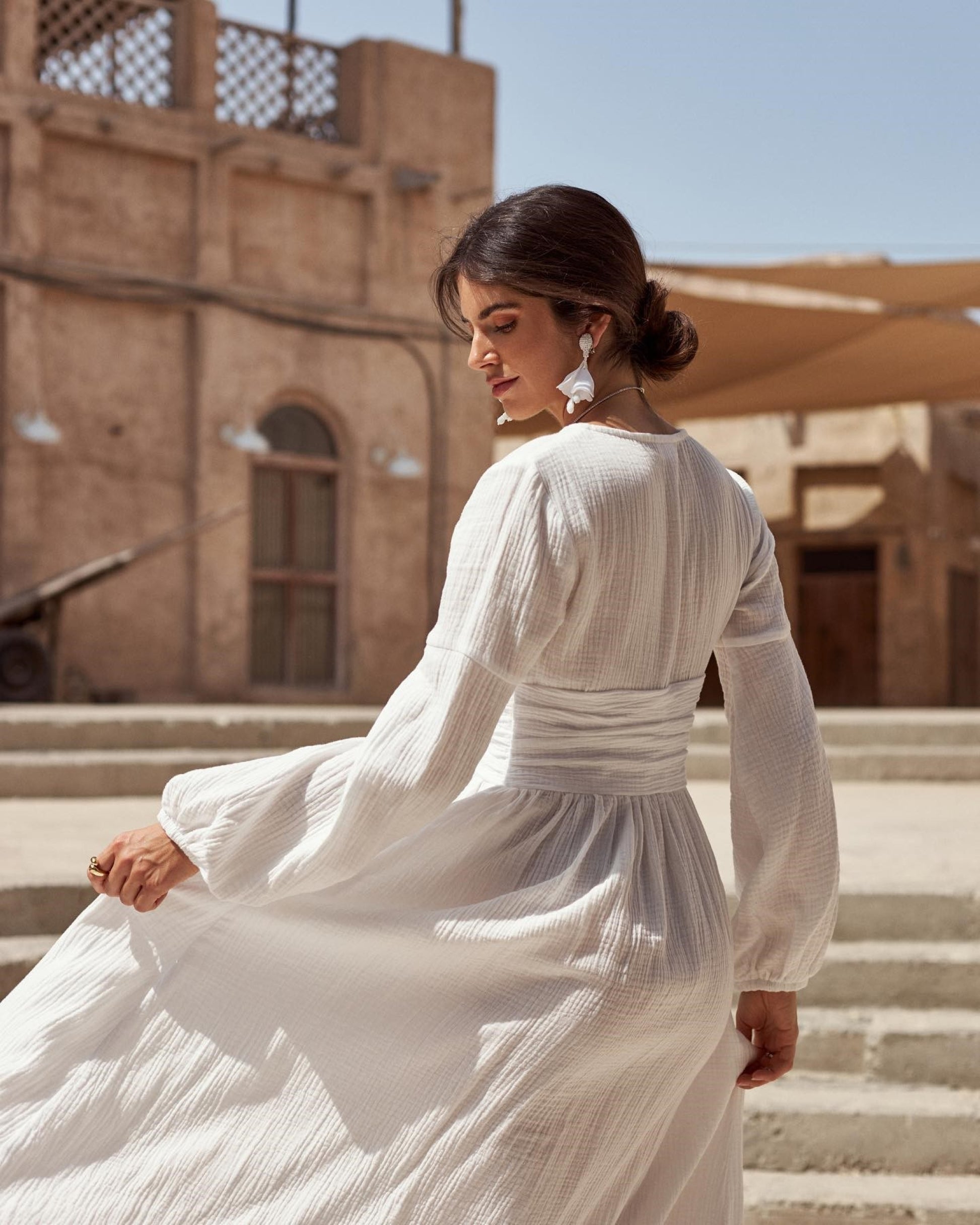 Woman in a white dress sitting on steps with a desert building in the background