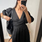 A woman takes a mirror selfie wearing a black midi wrap dress with puffed sleeves.